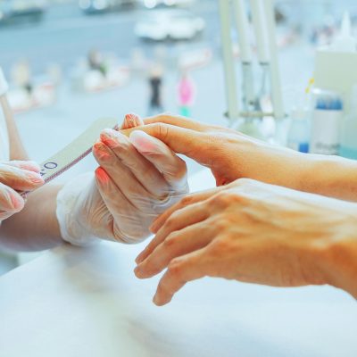 Close-up of a manicurist performing a nail file treatment on a customer's hand in a salon.