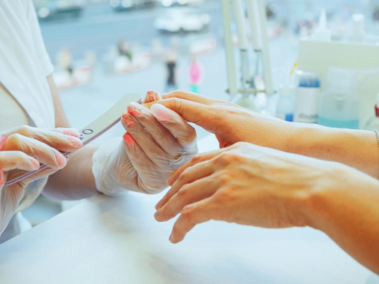 Close-up of a manicurist performing a nail file treatment on a customer's hand in a salon.