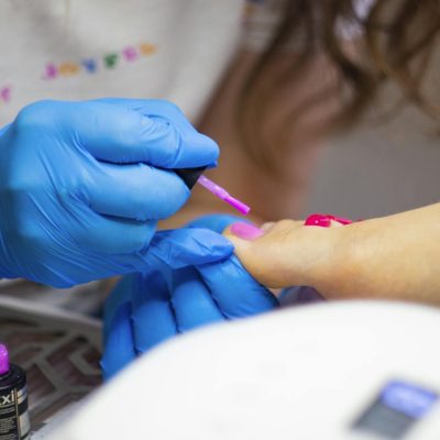 Detailed close-up of a pedicure session with blue gloves applying pink nail polish.