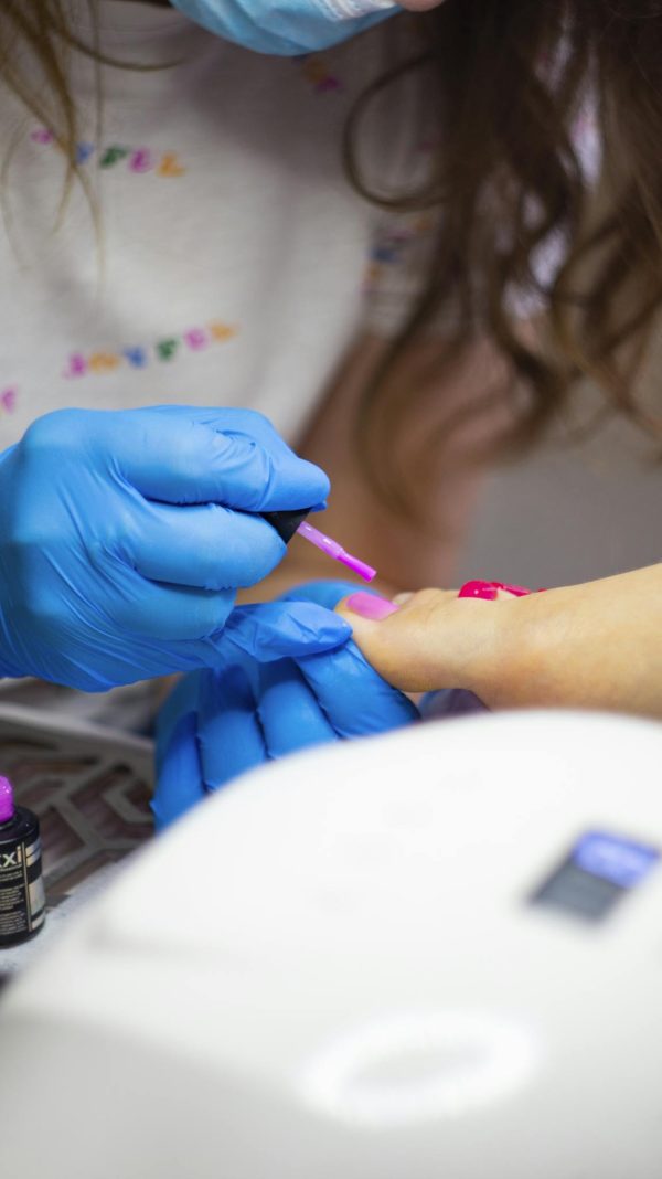 Detailed close-up of a pedicure session with blue gloves applying pink nail polish.